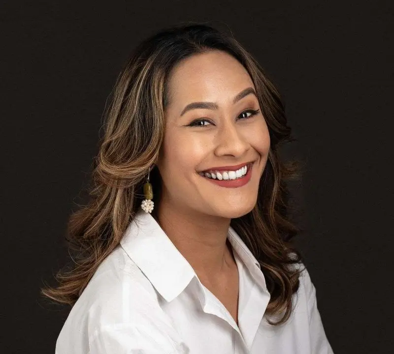Studio portrait of a smiling female emcee with long wavy hair in a white shirt